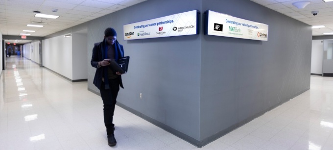 A student walks past the Partners in Management wall, with a long screen displaying logos of organizations the School of Management collaborates with. 