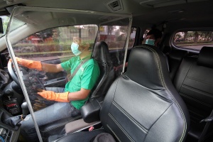 A Grab driver behind the wheel, wearing gloves and a face mask. Access a larger version of this image. 