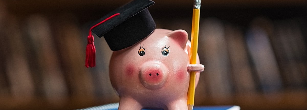Piggybank with graduation cap and pencil standing on notebooks. 