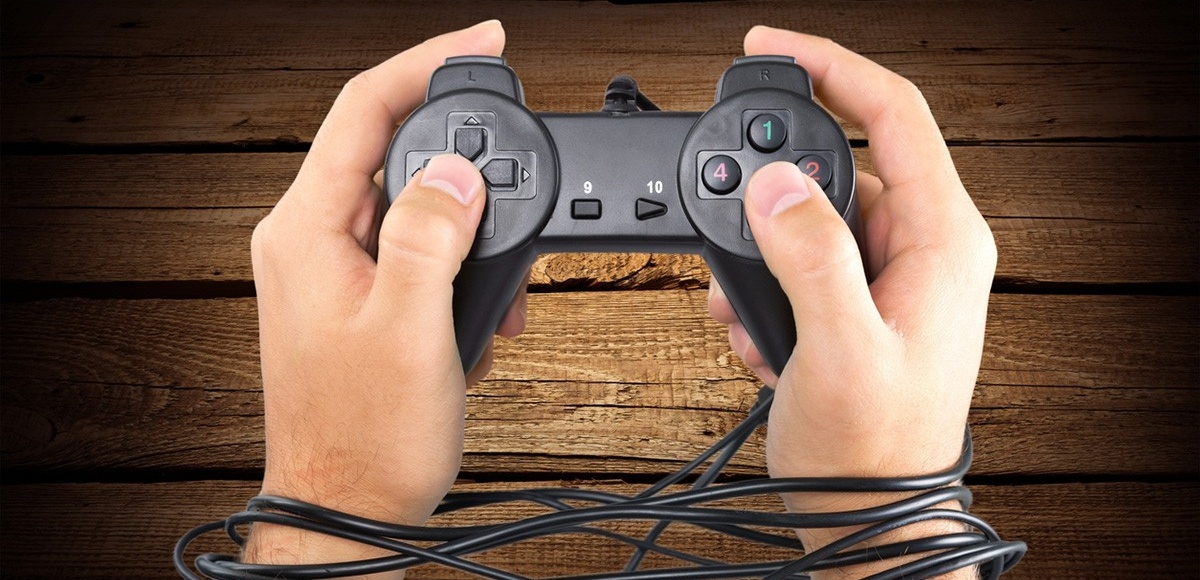 Two hands holding a video game controller with wrists bound by the cord. 