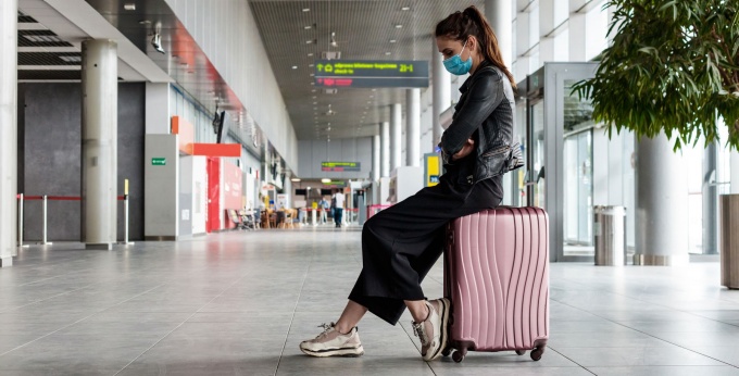 Woman wearing a mask sits with her luggage in an empty terminal. 