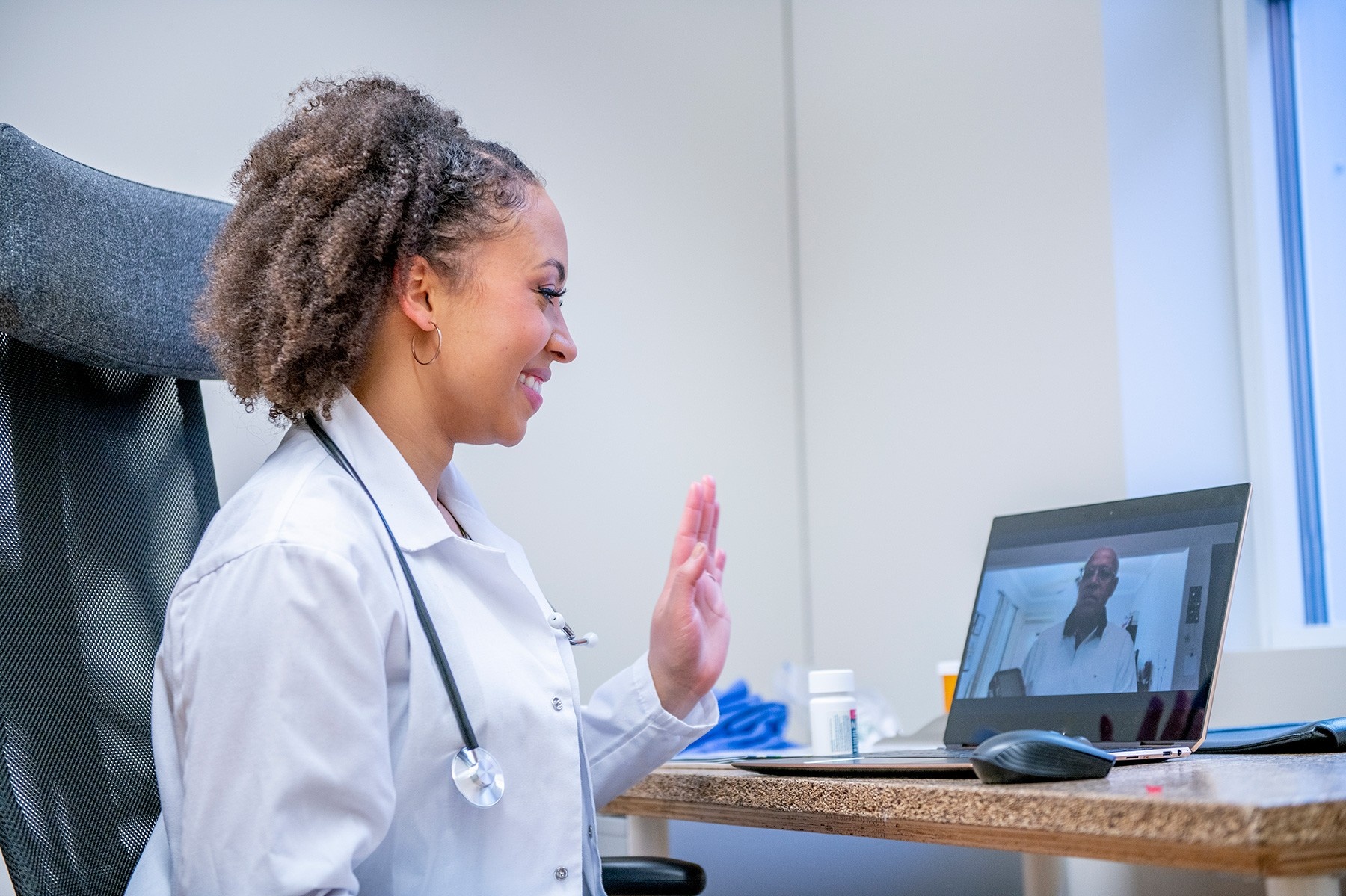 Doctor waving at patient on computer during telemedicine call. 