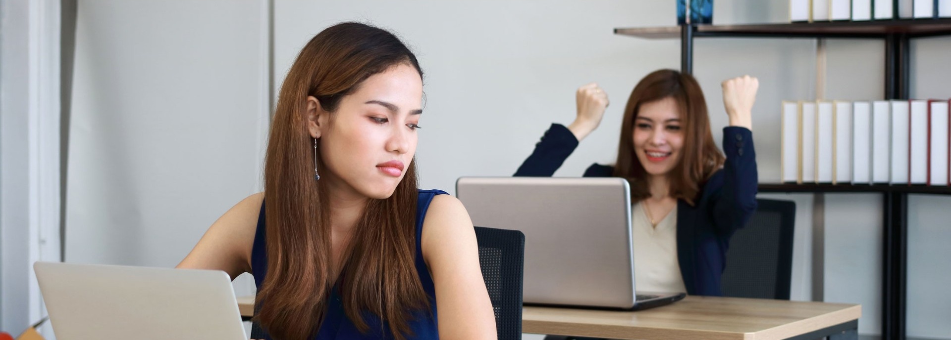 Coworker at desk looking over her shoulder in envy at employee behind her. 