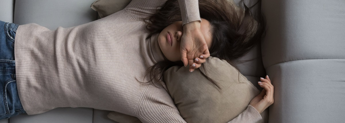 Woman laying on a couch with her arm over her eyes. 