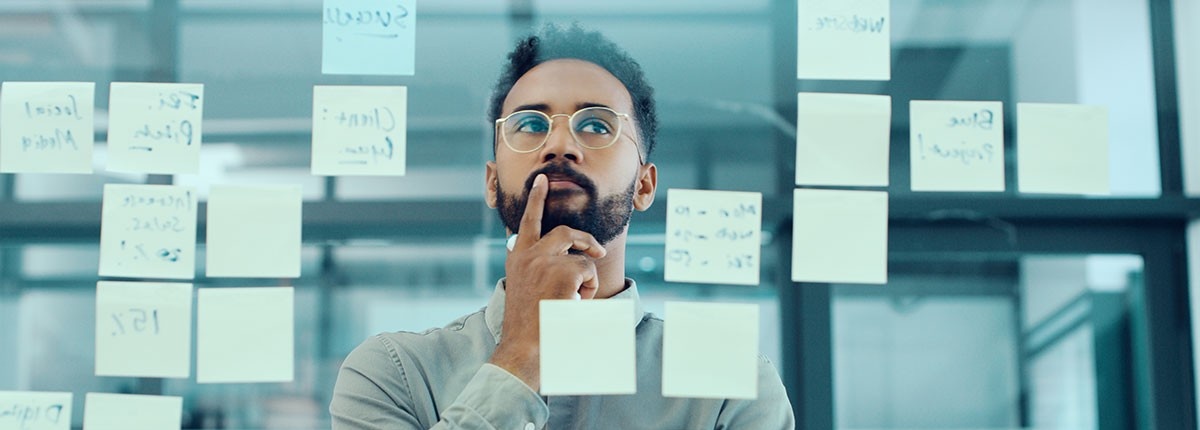 Business person looks at post-its on glass. 