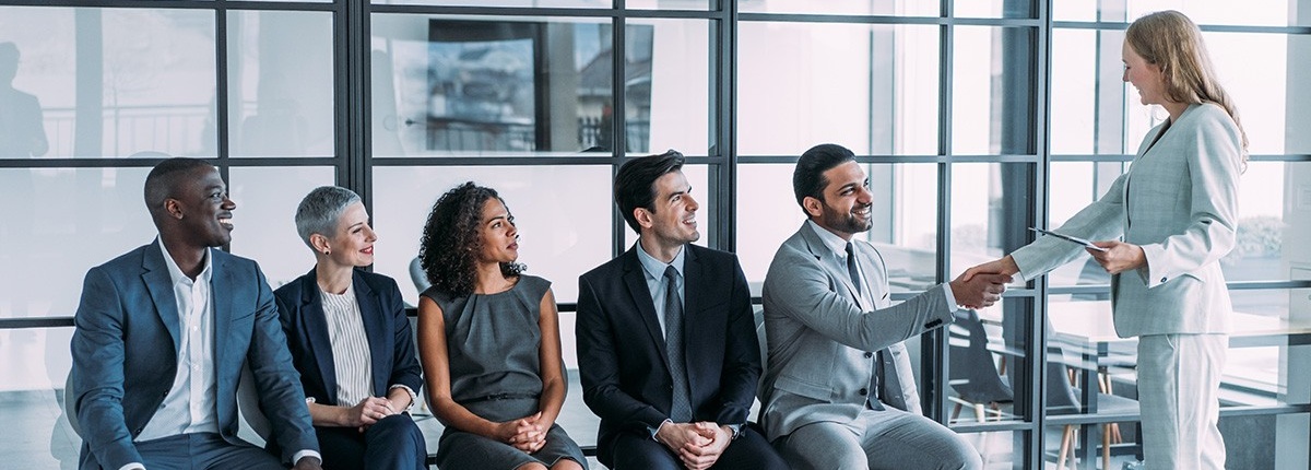 Shot of recruiter shaking hands with male job applicant. Group of business people waiting in line for job interview in modern office. 