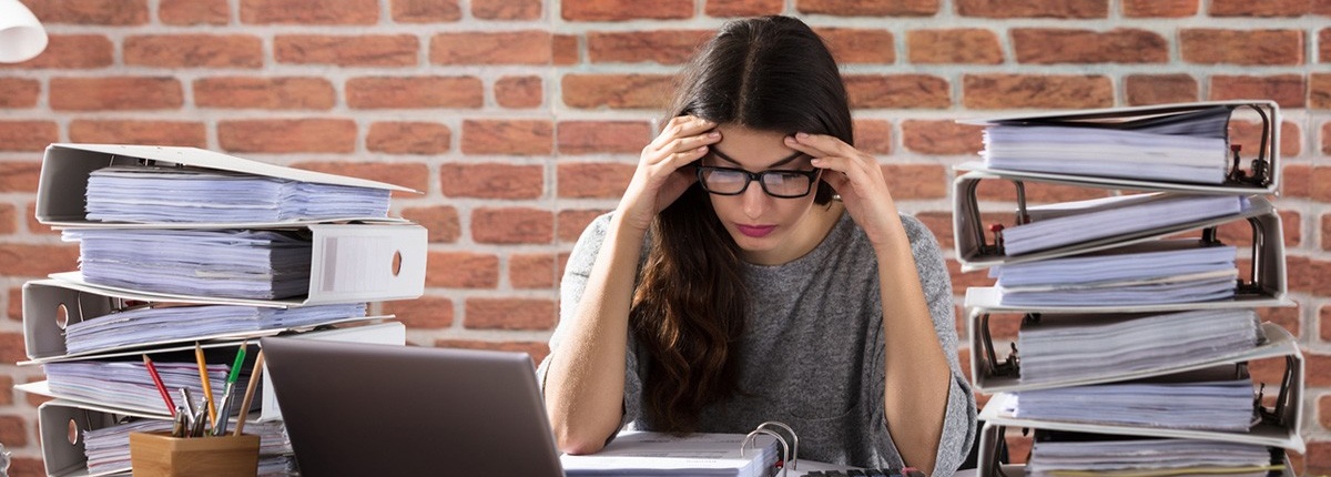 Stressed out woman surrounded by stacks of binders. 