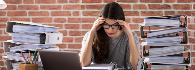 Stressed out woman surrounded by stacks of binders. 