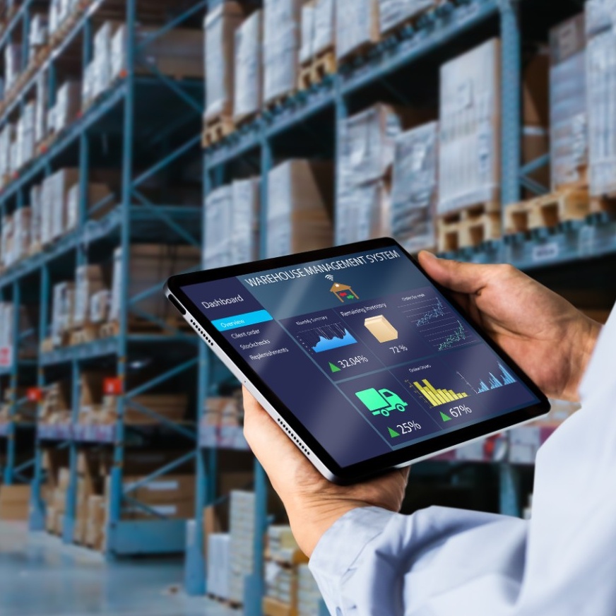 Worker in a warehouse holding a tablet displaying data. 