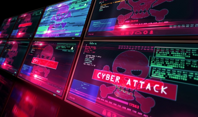 Multiple computer monitors display red cybersecurity alerts, skull-and-crossbones symbols, computer code, and the words “CYBER ATTACK.”. 