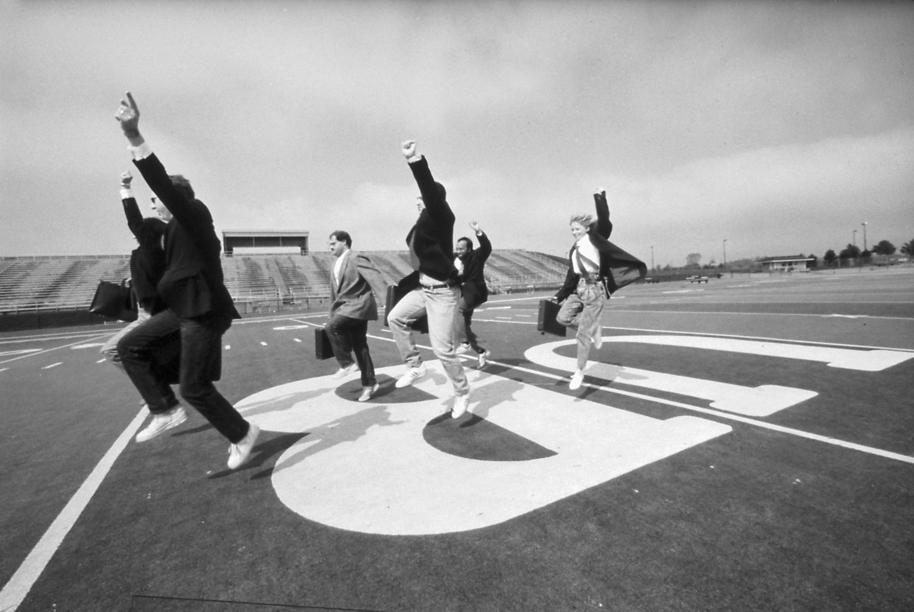 Zoom image: Not so serious business (1990): Members of the School of Management Precision Briefcase Marching Drill Team practice their routine for the Buffalo St. Patrick's Day Parade. Sporting the "modified IBM look" with white shirts, red ties, blue jackets, blue jeans, sneakers and sunglasses, the 18- to 25-member team of undergraduate and graduate students, faculty and alumni swung their briefcases down Delaware Avenue to the tunes "Taking Care of Business" and "Working for a Living." 