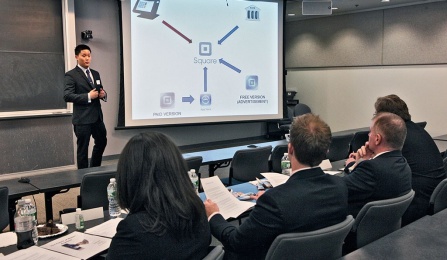 Student giving a presentation in a classroom in front of other students. A PowerPoint slide is on the screen. 