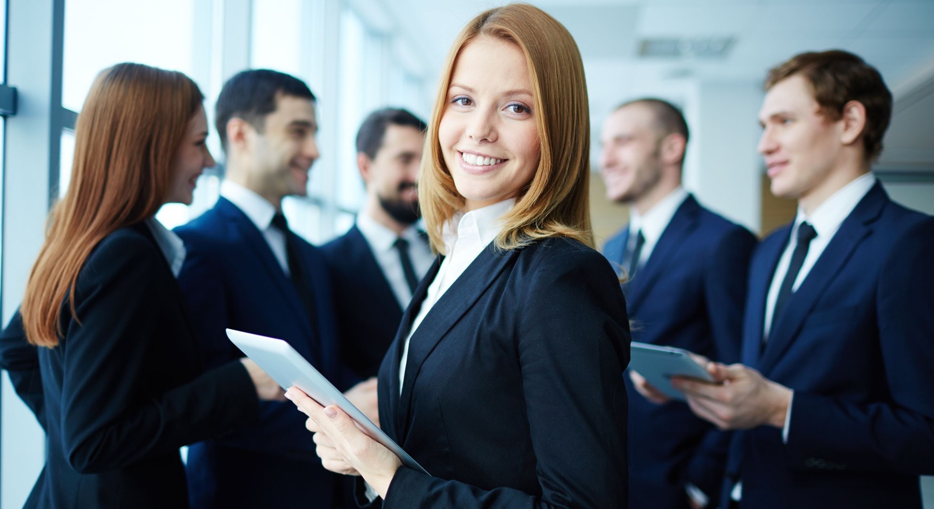 Group of students wearing dark suits, holding tablets. 