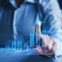 Person touching a transparent screen displaying stocks going up. 
