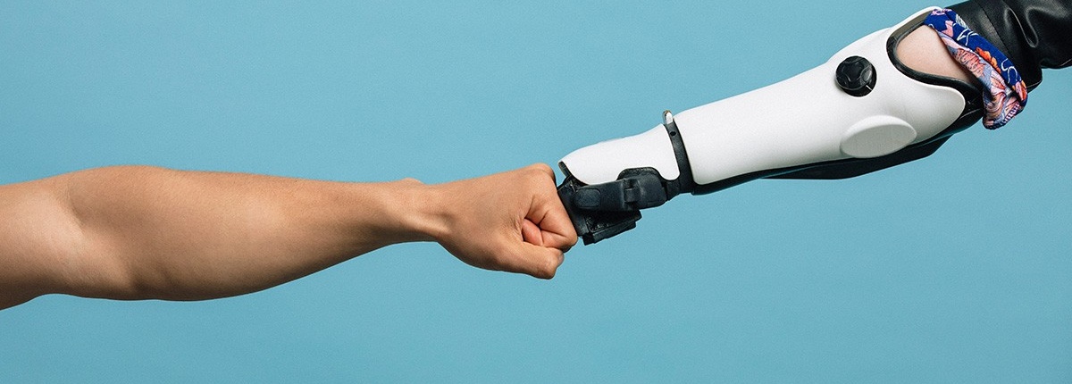 Photo of a human arm fist bumping a robotic arm. 