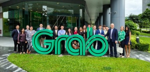 Students stand around sign that reads "GRAB" outside the company headquarters building. 