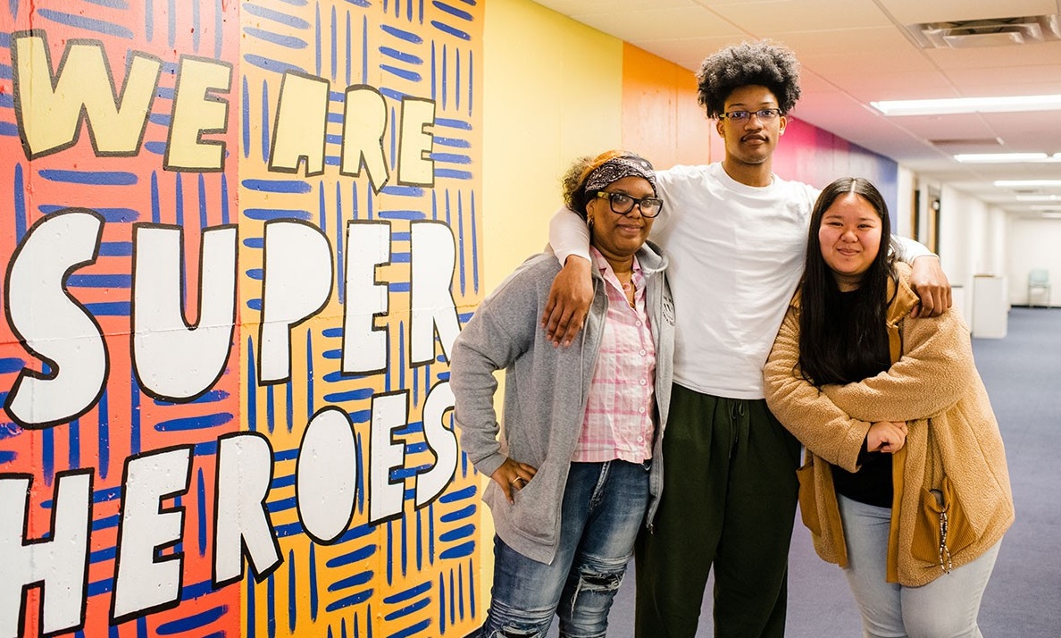 Group of three Buffalo Prep students by a wall that reads "we are super heroes.". 