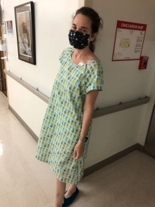 Diana Donnarumma stands in a hospital wearing a hospital gown with a colorful pineapple print. 