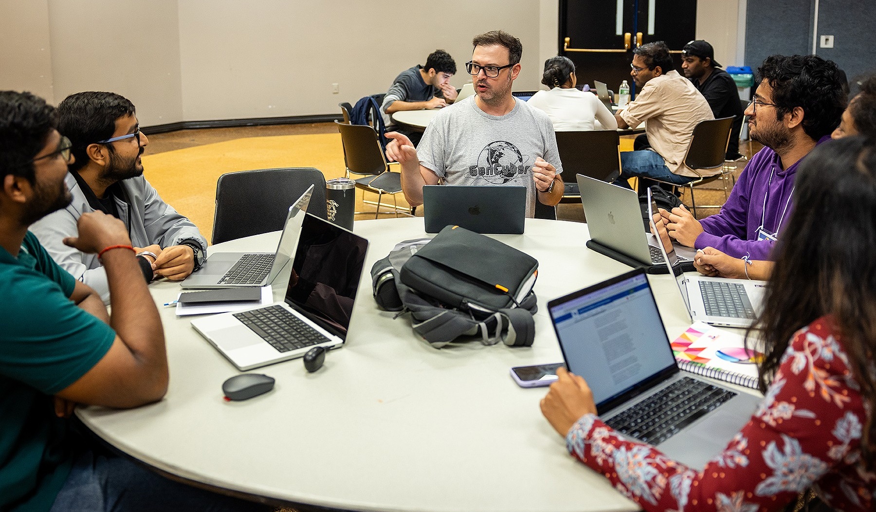 Students seated at a table listening to a mentor seated in the center of the group. 