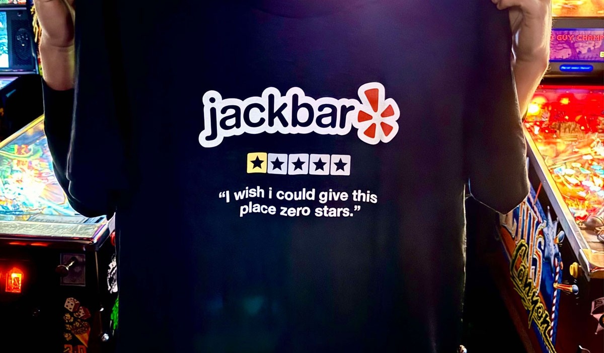 Person holds up a Yelp parody shirt in front of pinball machines. 