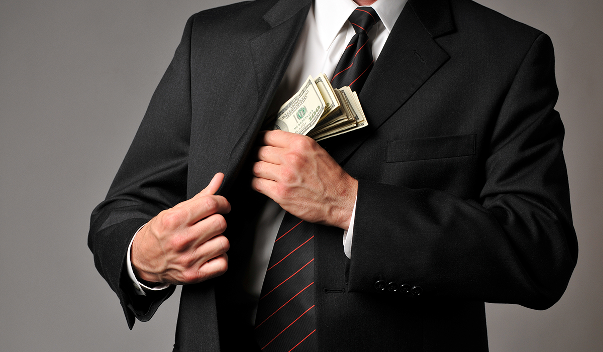 Businessperson stuffs cash into suit pocket. 