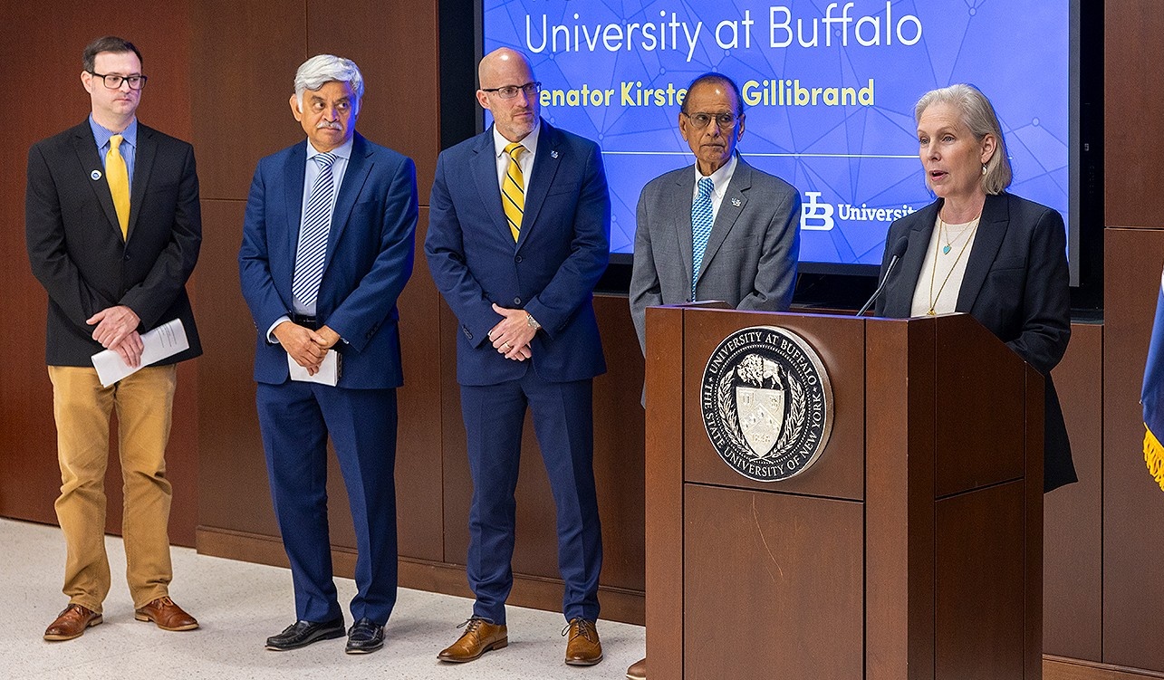 Gillibrand speaking at a lectern as university leaders stand by. 