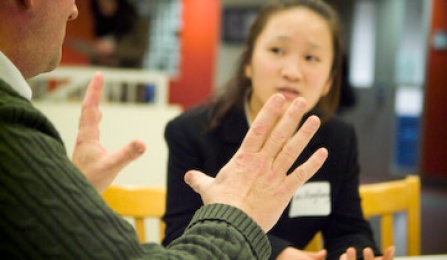 Business student sitting at table listening to advice from an alumnus. 