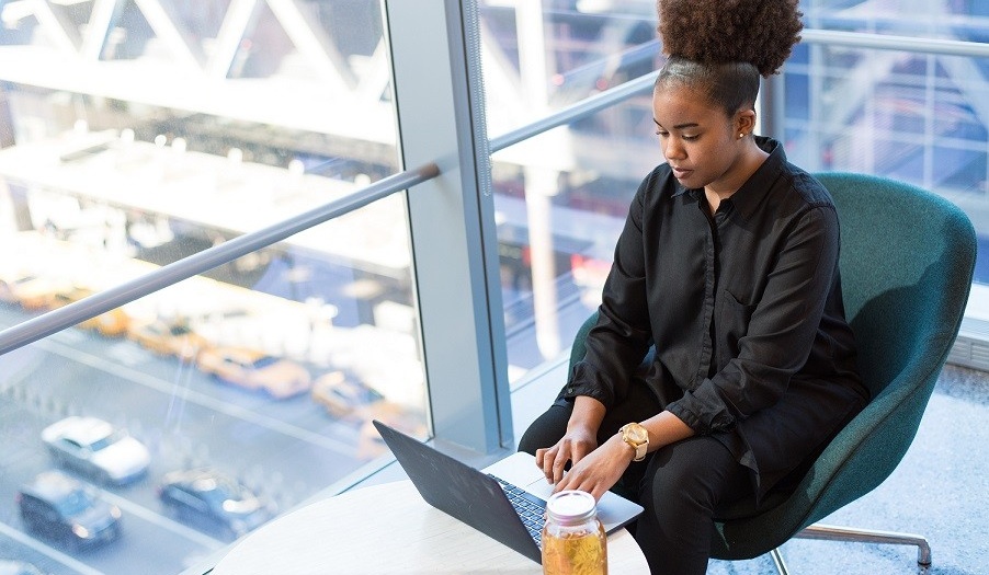 Individual working at laptop in glass-walled building.