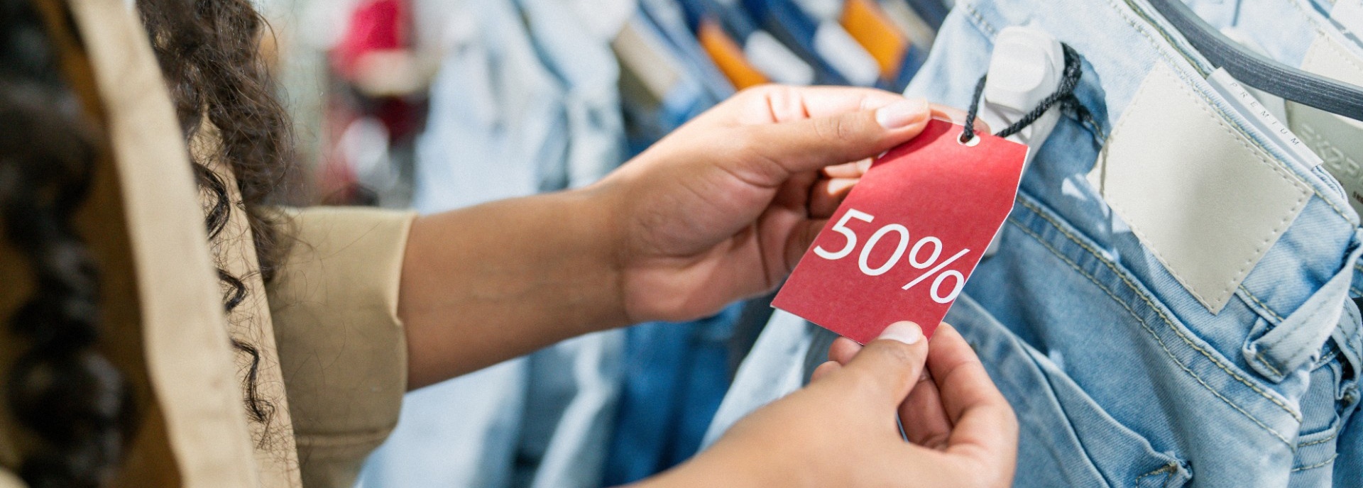 Hands holding a red tag on a pair of jeans marked 50% off.