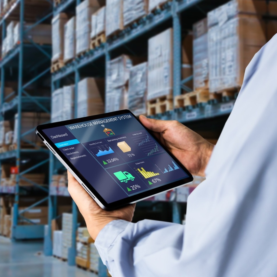 Person holding an ipad showing a dashboard while standing in a warehouse. 