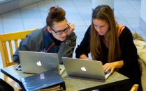 Two students sitting at a desk looking at laptop computers. 
