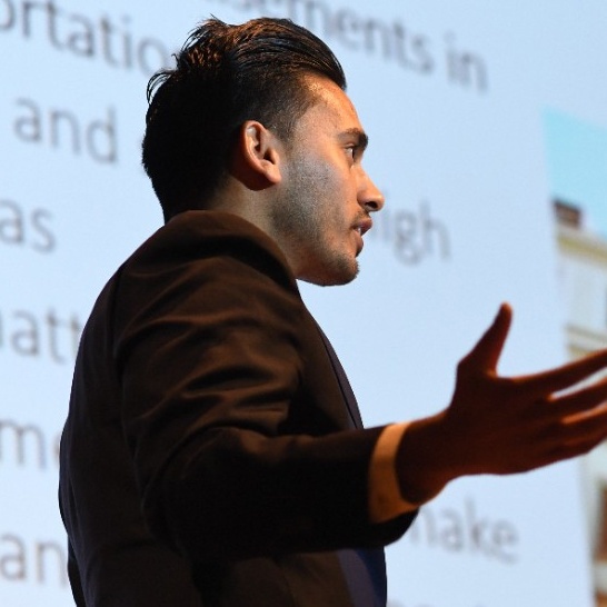 Male MBA student making a presentation to the side of a large projection screen. 