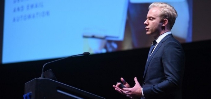 Male student in business attire presenting onstage. 