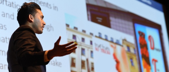 Male MBA student making a presentation to the side of a large projection screen. 