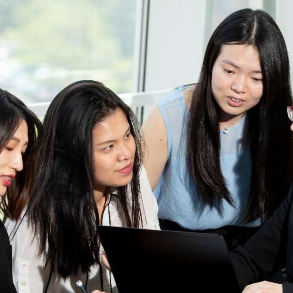 Four Asian School of Management students talking with each other behind a laptop computer. 