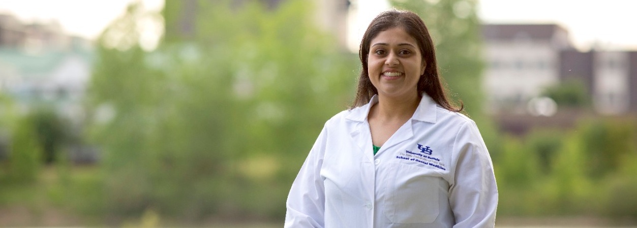 Dental student standing in white lab coat with trees in the background. 