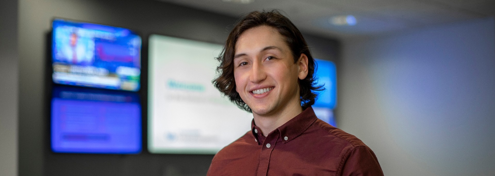School of Management Master's student standing in front of digital display boards.