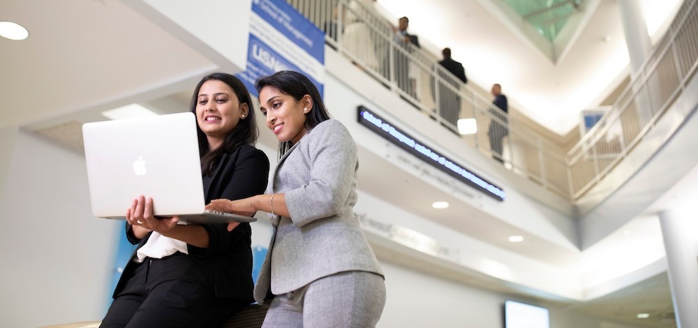 Two female MS Finance students looking at a laptop in Alfiero Center. 