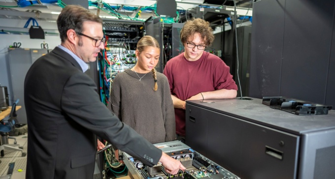 Male and female MIS students learning from professor in server room. 