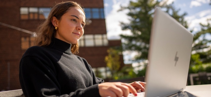 School of Management graduate student sitting outside typing on a laptop. 