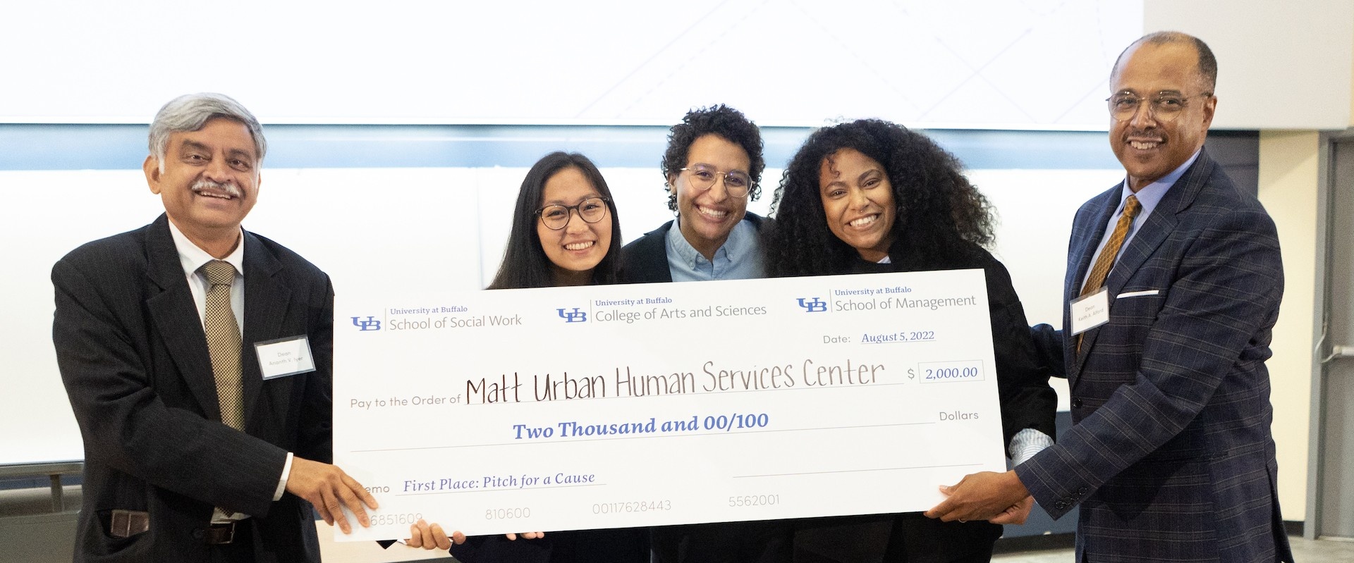 Three School of Management graduate students, 2022 winners of the Pitch for a Cause competition holding a large $2000 check, with Dean Iyer. 