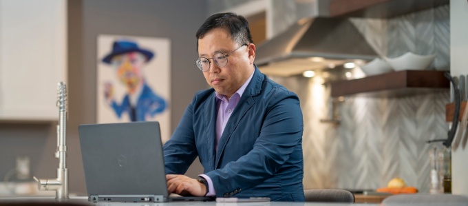 School of Management graduate student working on a laptop in a kitchen. 