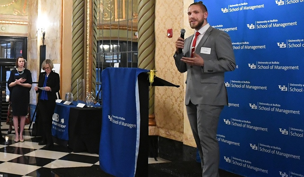 Zoom image: Student speaking at an event by the School of Management lectern banner.