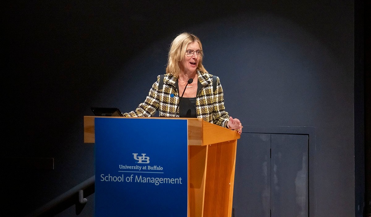 Zoom image: Alumna speaking at an event behind a lectern featuring the School of Management lectern sign.